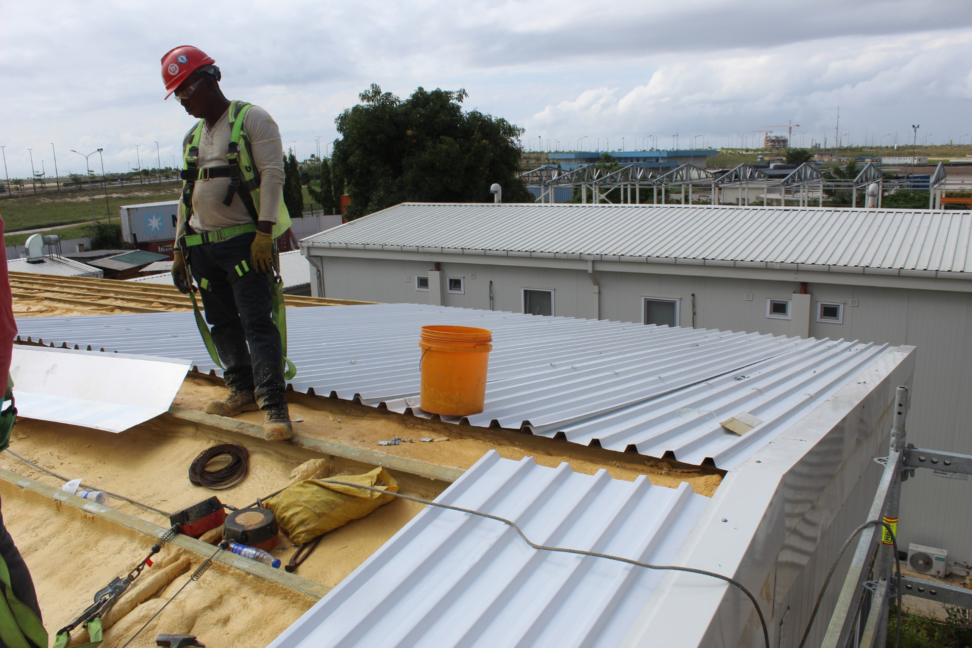 Worker in safety harness laying roof panels over spray foam insulation